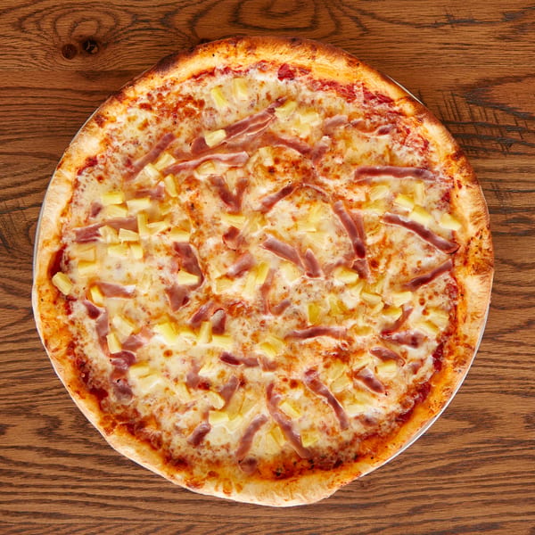 Hawaiian pizza topped with melted cheese, ham, and pineapple on a wooden table.