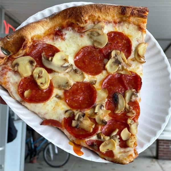 Large slice of pizza with pepperoni and mushrooms on a white paper plate.