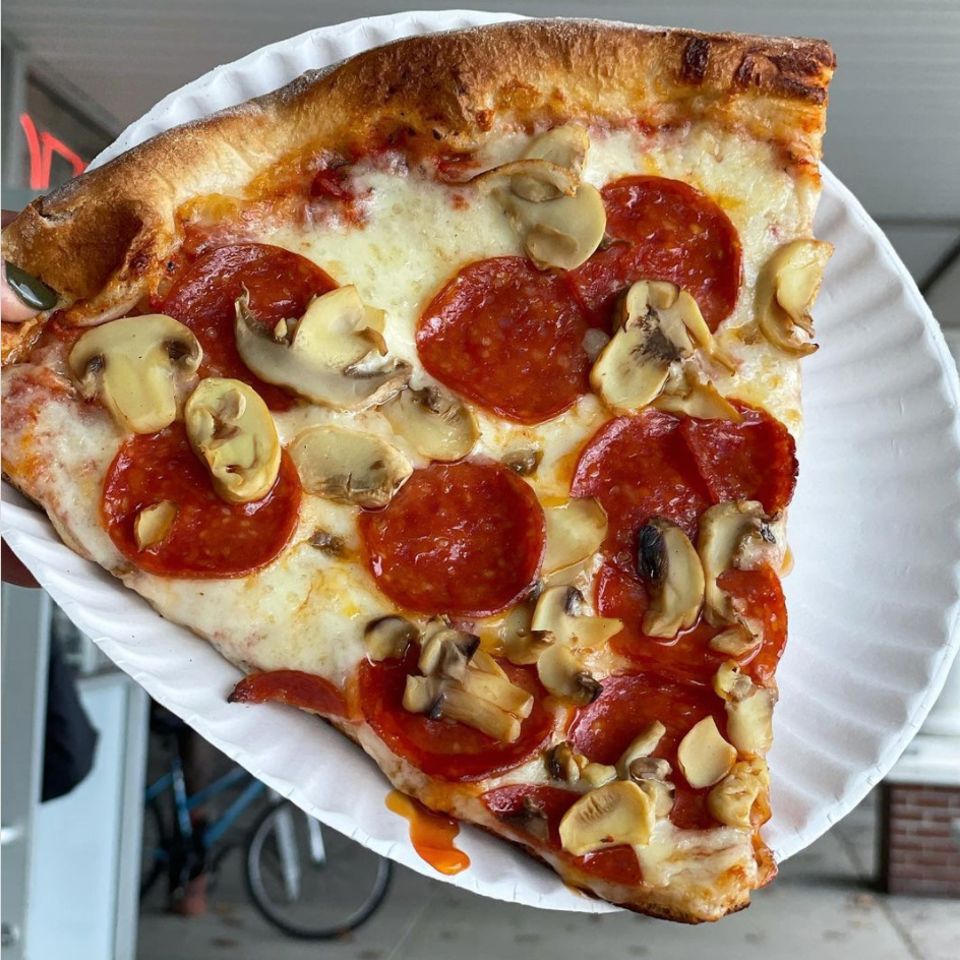Large slice of pizza with pepperoni and mushrooms on a white paper plate.