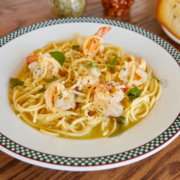 Shrimp scampi pasta with basil and parmesan in a white bowl with a checkered rim.