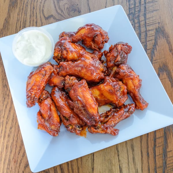 A white square plate filled with barbecue chicken wings and a side of ranch dressing.