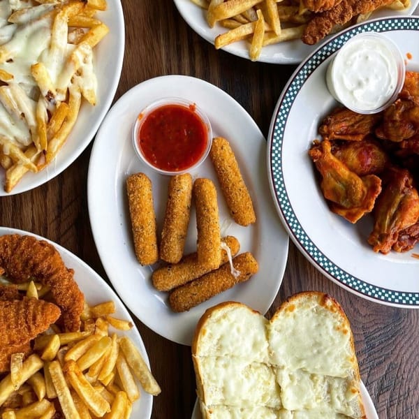 An overhead view of various appetizers including fries, mozzarella sticks, chicken wings, and cheesy bread.