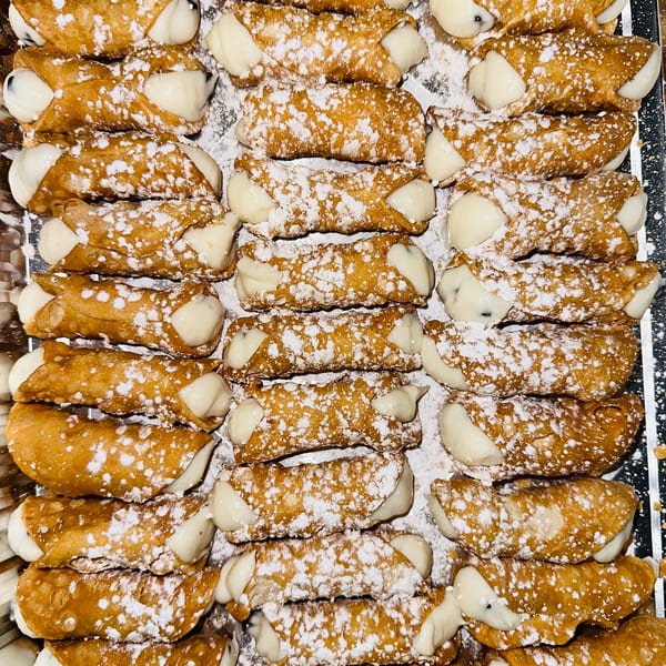 Golden-brown cannoli filled with white cream and dusted with powdered sugar, arranged in rows.