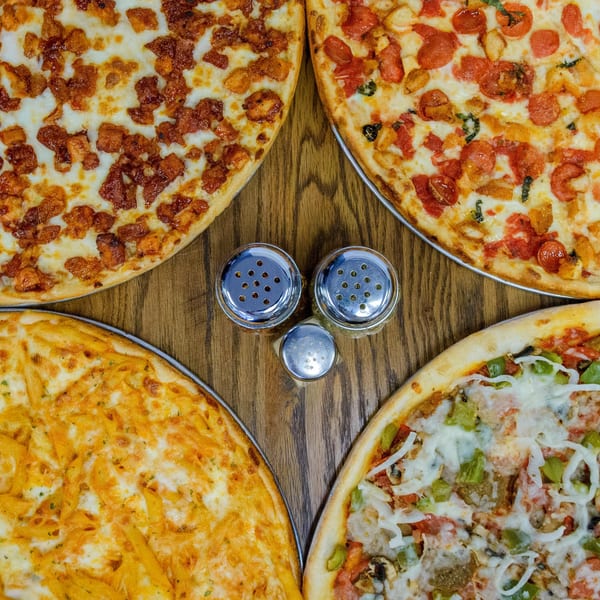 Four different pizzas and three spice shakers arranged on a wooden table.