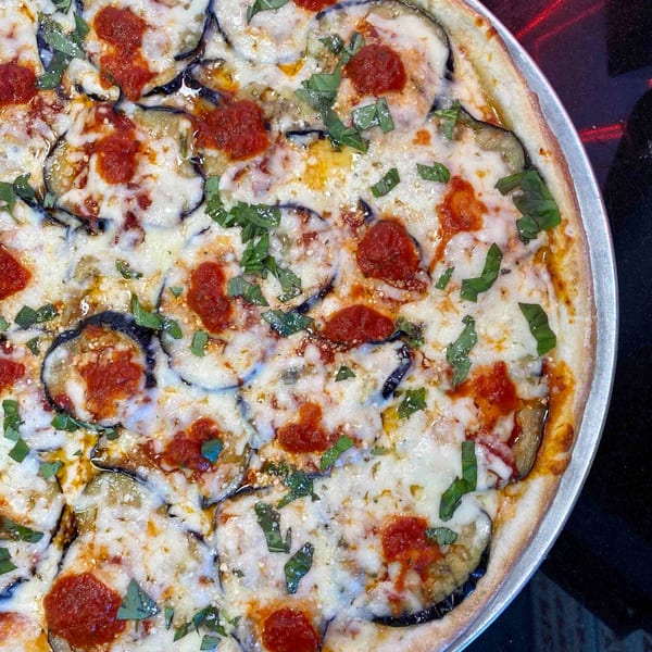 Eggplant pizza with melted cheese, tomato sauce, and fresh basil in a metal pan.